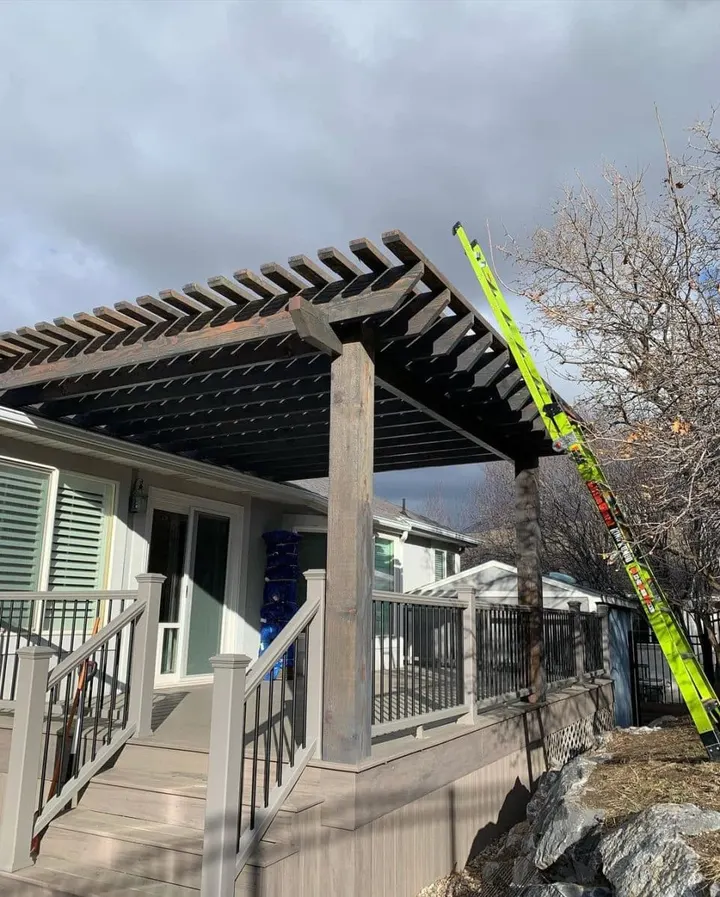 Dark open-lattice pergola under construction over a deck