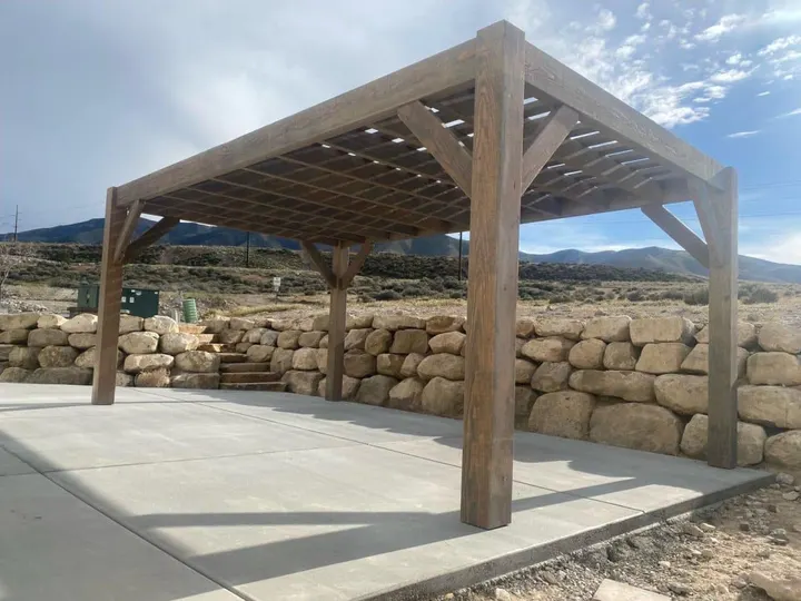 Freestanding open-lattice pergola beside a stone retaining wall