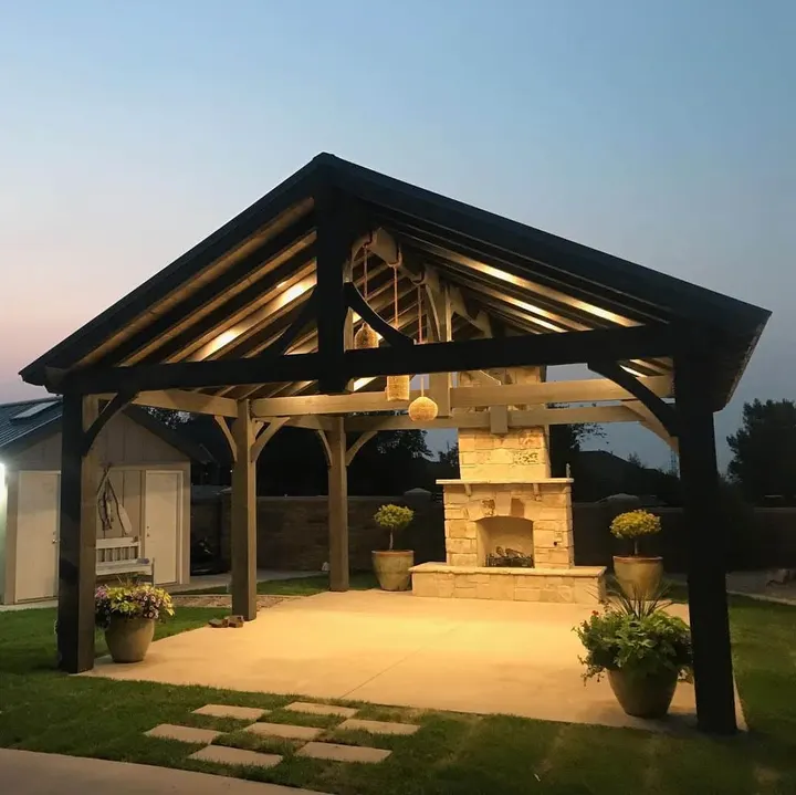 Gabled pavilion with an illuminated stone fireplace at dusk