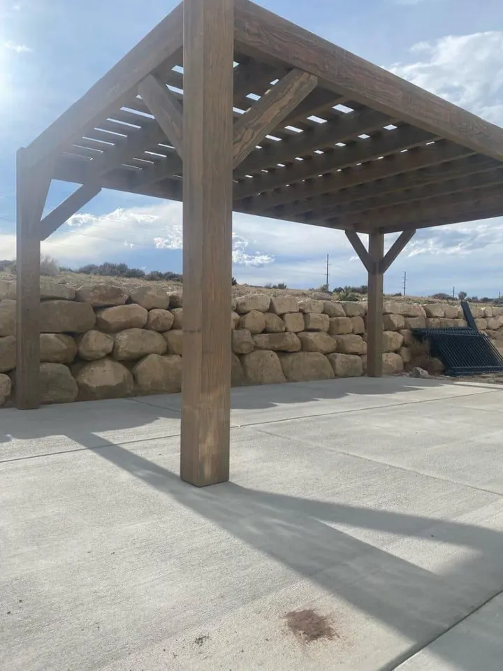 Pergola posts over a concrete patio beside a retaining wall
