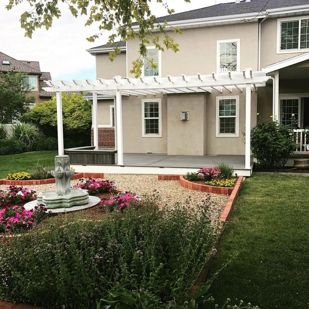 White timber pergola beside a garden fountain and flower beds